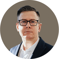 Person wearing glasses and a suit, posing against a plain background.